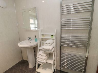 A bathroom with a pedestal sink mirror shelf towel rack and a ladder shelf with towels and toiletries at Barnacre in Longhirst near Morpeth