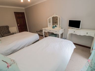 A bedroom with two single beds a dressing table a television and an armchair at Barnacre in Longhirst near Morpeth