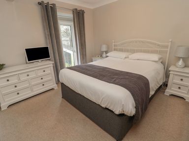A bedroom with a double bed two bedside tables with lamps a chest of drawers with a television and curtains at Barnacre in Longhirst near Morpeth