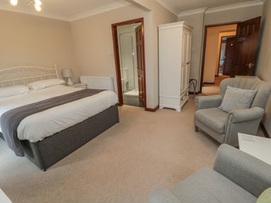 A bedroom with a bed a bedside table with lamp an armchair a wardrobe and an en suite bathroom at Barnacre in Longhirst near Morpeth