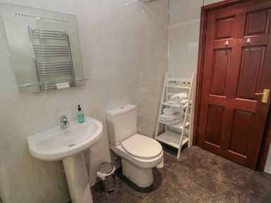 A bathroom with a pedestal sink a toilet a small rack with towels and toiletries and a wooden door at Barnacre Longhirst near Morpeth