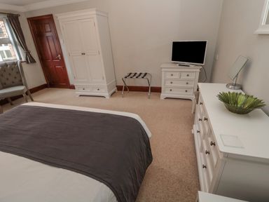 A bedroom with a bed a white wardrobe a chest of drawers a television a chair and a luggage rack at Barnacre Longhirst near Morpeth