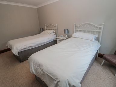A bedroom with two single beds white bed frames a nightstand with two lamps and a chair at Barnacre in Longhirst near Morpeth