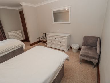 A bedroom with two beds a white dresser a mirror a gray chair and a trash bin at Barnacre Longhirst near Morpeth