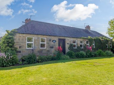 A stone house with a slate roof surrounded by plants and flowers in a garden at Barnacre in Longhirst near Morpeth