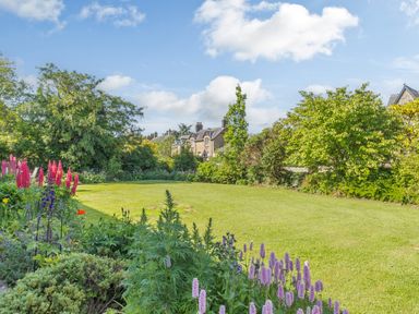 A garden with green grass surrounded by flowers and trees at Barnacre Longhirst near Morpeth
