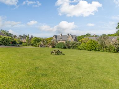 A large green lawn with a wooden picnic table and houses with slate roofs in the background at Barnacre in Longhirst near Morpeth