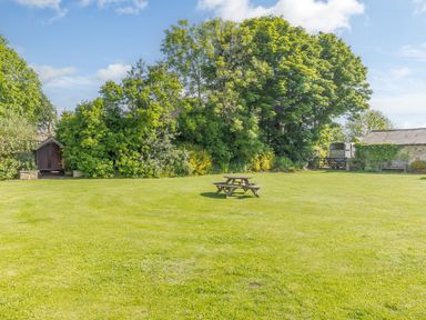 A grassy garden with a wooden picnic table surrounded by trees and shrubs at Barnacre in Longhirst near Morpeth