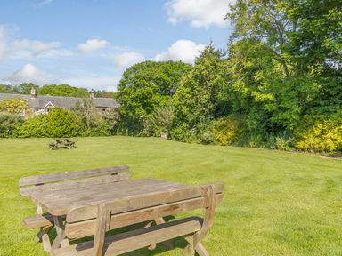 A wooden picnic table on a grass lawn with trees and houses in the background at Barnacre in Longhirst near Morpeth