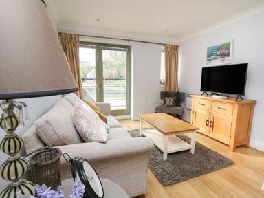 A living room with a sofa cushions wooden coffee table and television on a wooden cabinet at Flat 2 in Pembroke