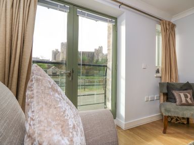 A living room with a sofa and chair near a glass door showing a castle outside at Flat 2 in Pembroke