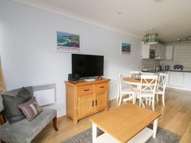 A living area with a wooden cabinet holding a TV a round dining table with four chairs a couch with cushions and a wooden coffee table at Flat 2 in Pembroke