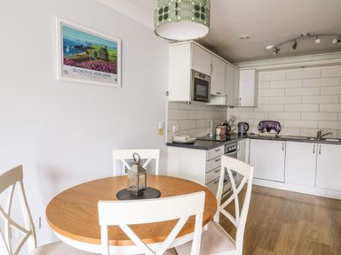 A kitchen with white cabinets and a round wooden dining table with white chairs at Flat 2 in Pembroke