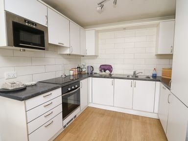 A kitchen with white cabinets black countertop built in oven and microwave at Flat 2 in Pembroke