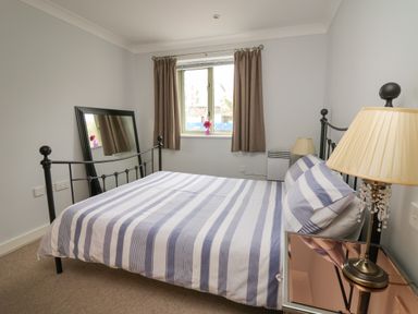 A bedroom with a striped bedspread a mirror leaning against the wall and a lamp on a bedside table at Flat 2 in Pembroke