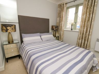 A bedroom with a striped bedspread two bedside tables with lamps and a window with curtains at Flat 2 in Pembroke