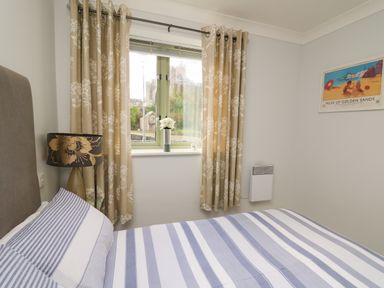 A bedroom with a bed with striped bedding a window with patterned curtains a floral lamp and a framed picture on the wall at Flat 2 in Pembroke