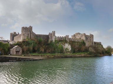 A large stone castle on a hill beside a river with a small building and dock at Flat 2 in Pembroke