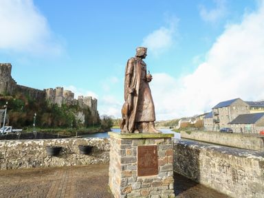 A statue of King Henry VII with a castle and river in the background at Flat 2 in Pembroke