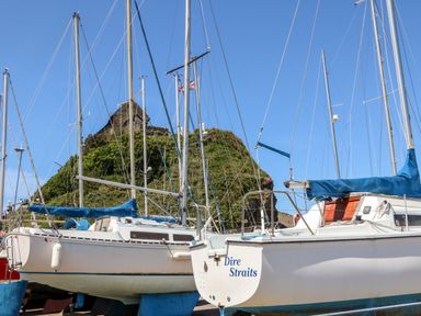Sailboats docked near a green hill with a small stone building on top at 65 Channel View in Ilfracombe