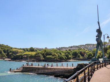 A waterfront promenade with a statue holding a sword overlooking a pier and water at 65 Channel View in Ilfracombe