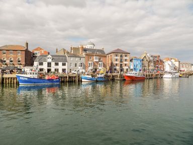A harbor with boats moored along the quay and buildings including a pub and cafes at The Chocolate Box in Weymouth