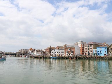A harbor with boats docked along the waterfront and buildings lining the shore at The Chocolate Box in Weymouth