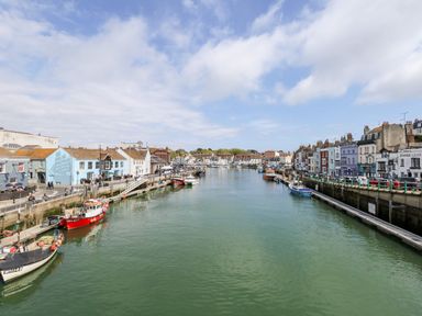 A harbor with fishing boats docked along both sides and buildings lining the waterfront at The Chocolate Box in Weymouth