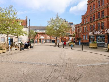 A paved public square with trees and benches surrounded by brick and stone buildings at The Chocolate Box in Weymouth