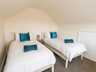 A bedroom with two single beds with white bedding and teal pillows and cushions at The Chocolate Box in Weymouth