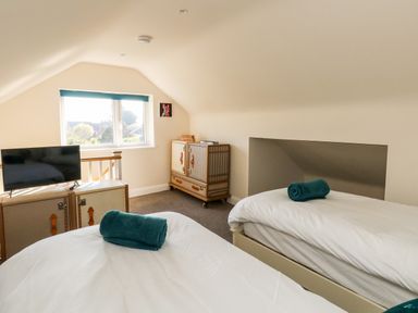 A bedroom with two single beds with rolled towels a TV on a cabinet a window and a cupboard at The Chocolate Box in Weymouth