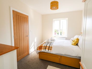 A bedroom with a bed, pillows, a window, a wooden door, and a dresser at The Chocolate Box in Weymouth