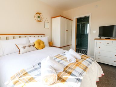 A bedroom with a bed with white linens and decorative pillows a wardrobe a dresser with a TV and a door leading to a bathroom at The Chocolate Box in Weymouth
