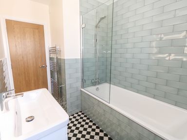 A bathroom with a bathtub shower combination white sink and wooden door at The Chocolate Box in Weymouth