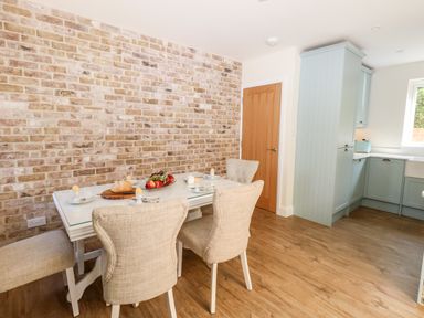 A dining area with a table set with egg cups and fruit next to a kitchen with blue cabinets at The Chocolate Box in Weymouth