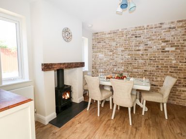 A dining area with a glass table and four chairs next to a wood burning stove and a brick wall at The Chocolate Box in Weymouth
