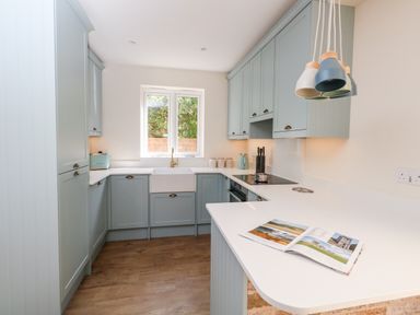 A kitchen with light blue cabinets a white countertop and a window above the sink at The Chocolate Box in Weymouth