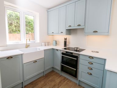 A kitchen with blue cabinets a white sink a stove an oven and a window at The Chocolate Box in Weymouth