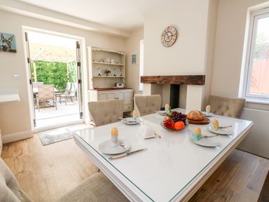 A dining room with a set table for breakfast and an open door leading to an outdoor patio at The Chocolate Box in Weymouth