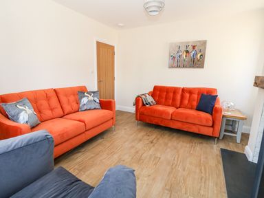 A living room with two orange sofas, a blue chair, a wooden door, and a painting of zebras at The Chocolate Box in Weymouth