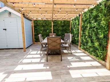 An outdoor dining area with a wooden pergola green walls and a set of table and chairs at The Chocolate Box in Weymouth