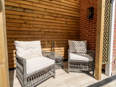 Two cushioned wicker chairs with a small wicker table between them on a wooden floored porch with wooden and brick walls at The Chocolate Box in Weymouth