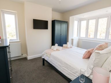 A bedroom with a bed facing a wall-mounted TV and a wardrobe by the window at The Chocolate Box in Weymouth
