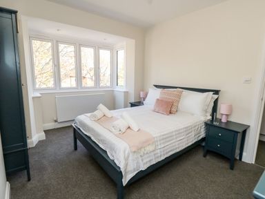 A bedroom with a bed with pillows and towels beside windows and bedside tables at The Chocolate Box in Weymouth