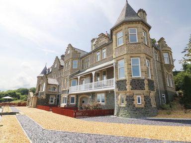 An exterior view of a large stone building with multiple windows and a balcony at On the Straits in Glyngarth near Menai Bridge