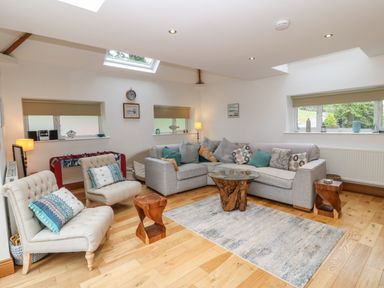 A living room with a grey sectional sofa two beige armchairs a glass and wood coffee table and wooden stools at On the Straits in Glyngarth near Menai Bridge
