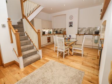 A kitchen with a round glass dining table and white chairs next to a carpet and staircase at On the Straits in Glyngarth near Menai Bridge