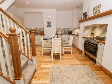 A kitchen with wooden flooring a glass dining table four chairs a staircase and an oven at On the Straits in Glyngarth near Menai Bridge
