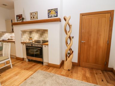 A kitchen area with a stainless steel stove and oven white cabinets wooden floor a wooden door and a carved wooden sculpture at On the Straits in Glyngarth near Menai Bridge