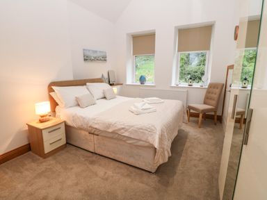 A bedroom with a double bed bedside table lamp chair and two windows at On the Straits in Glyngarth near Menai Bridge